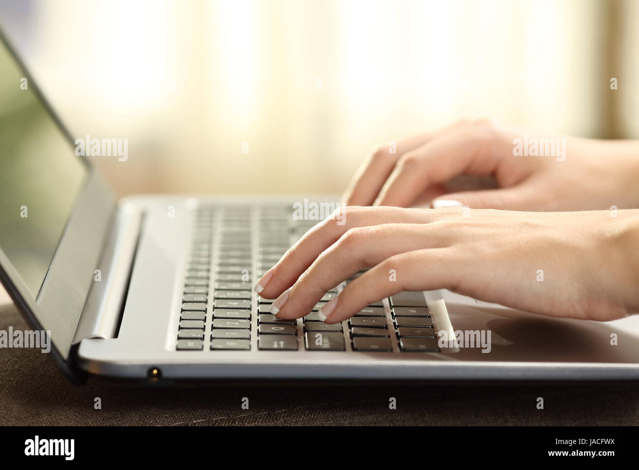 Close up of a woman mains tapant sur un clavier d'ordinateur portable avec une fenêtre et une lumière chaude dans l'arrière-plan Banque D'Images