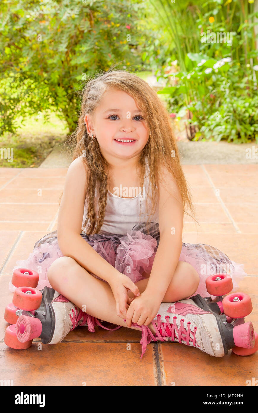 École maternelle Petite fille assise sur sol portant des patins à son  passage et ses jambes, dans un fond de jardin Photo Stock - Alamy