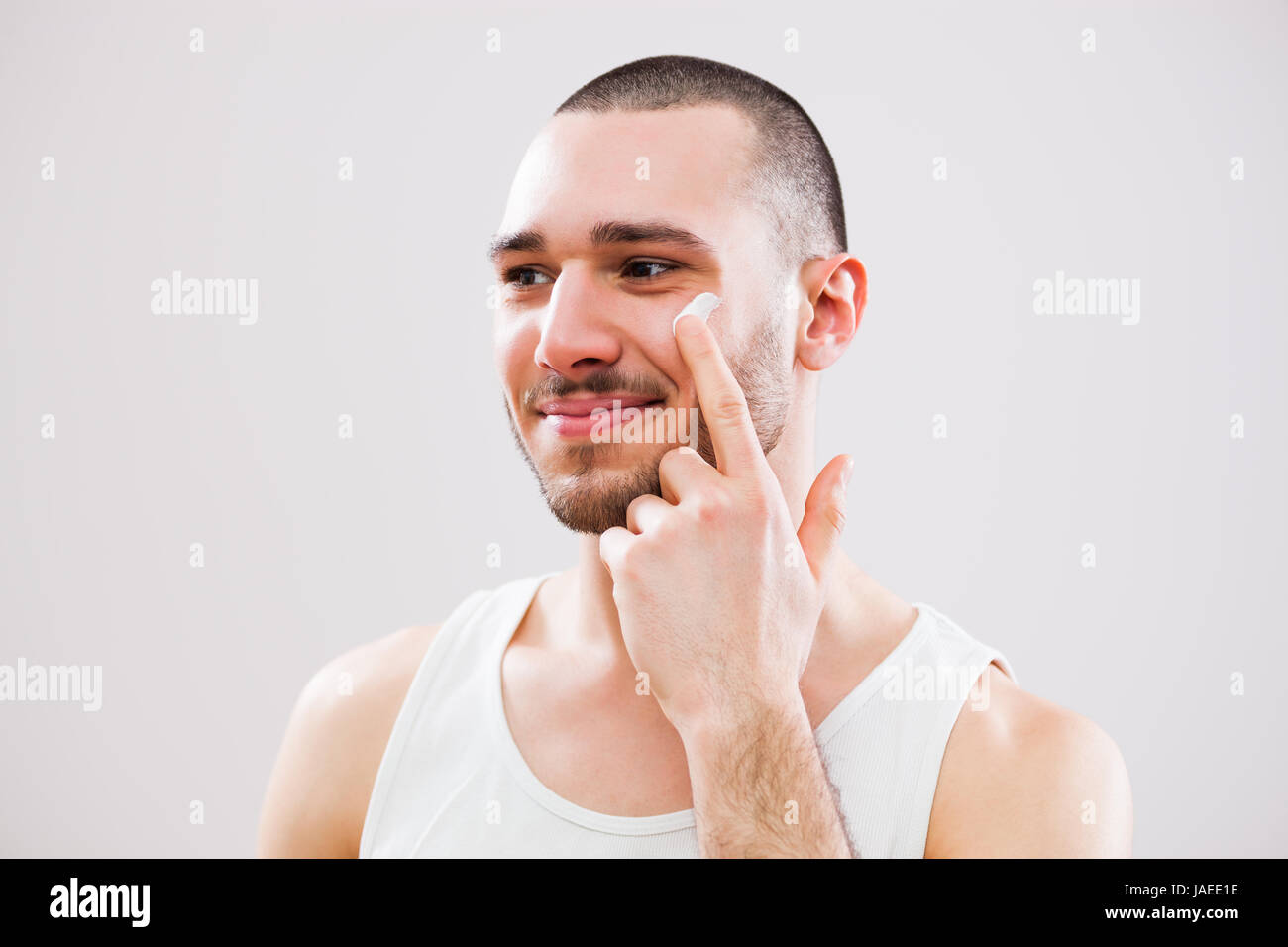 Jeune homme qui est l'application de la crème de peau sur son visage. Banque D'Images