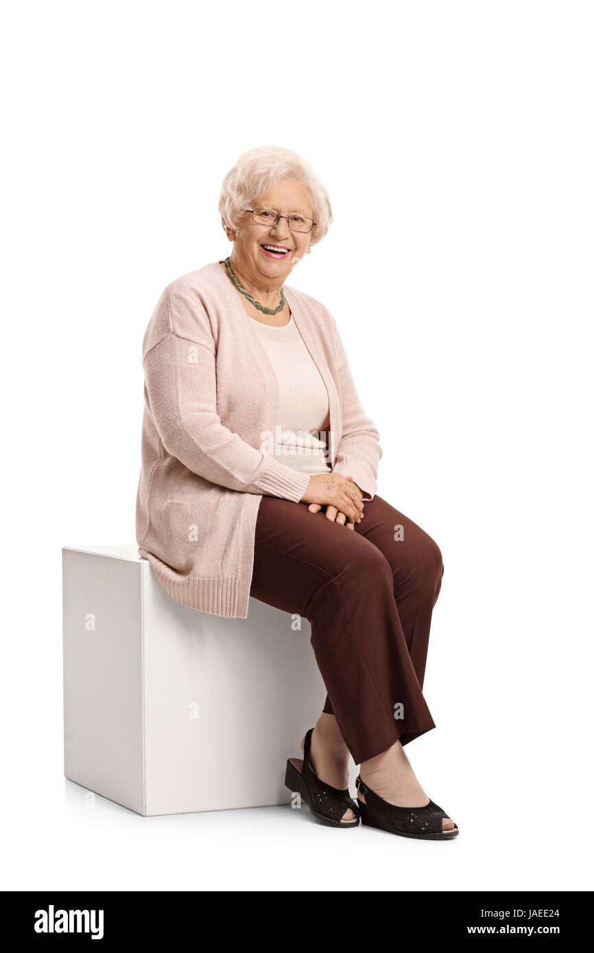 Femme âgée assise sur un cube regardant la caméra et smiling isolé sur fond blanc Banque D'Images