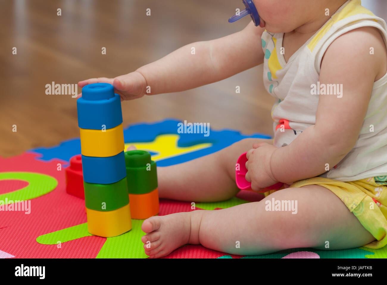 Tout-petit joue avec building block sur le tapis en caoutchouc de couleur. Banque D'Images