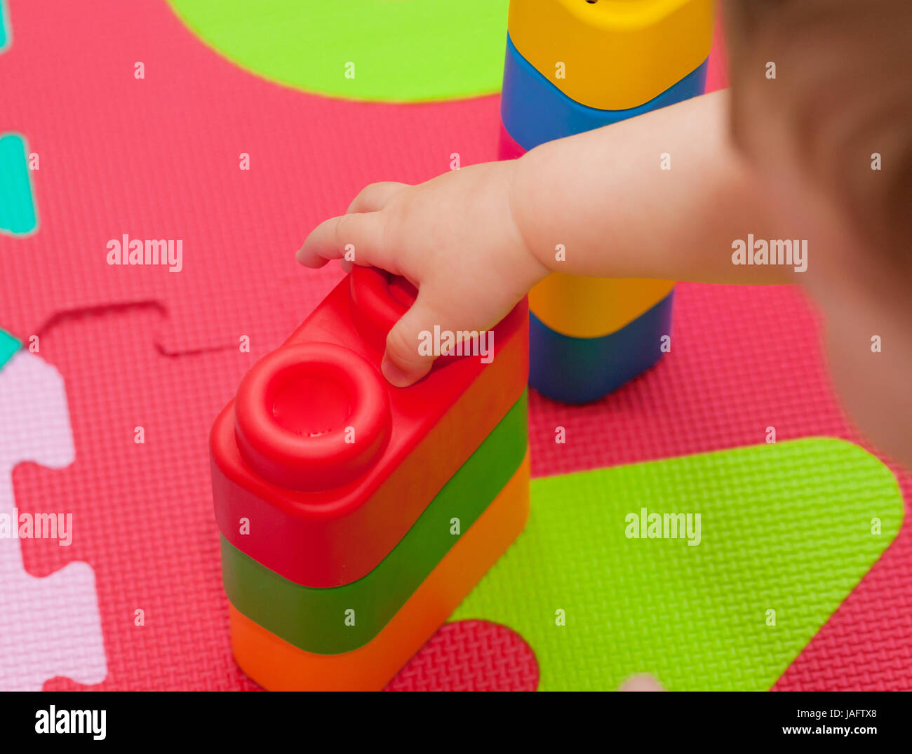 Tout-petit joue avec building block sur le tapis en caoutchouc de couleur. Banque D'Images