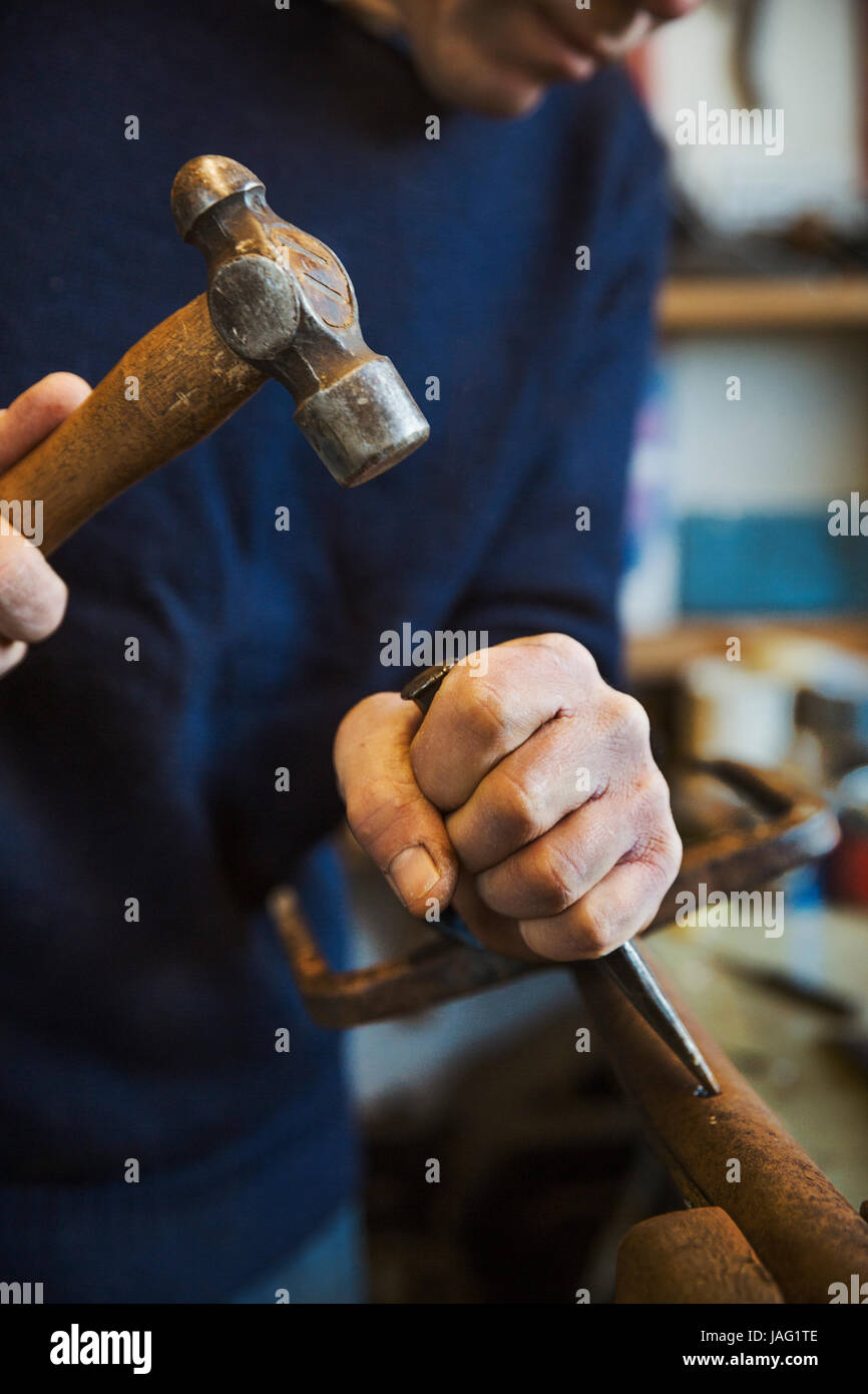 Homme debout, dans un atelier, tenant un marteau et ciseaux à bois, de travailler sur un morceau de bois. Banque D'Images