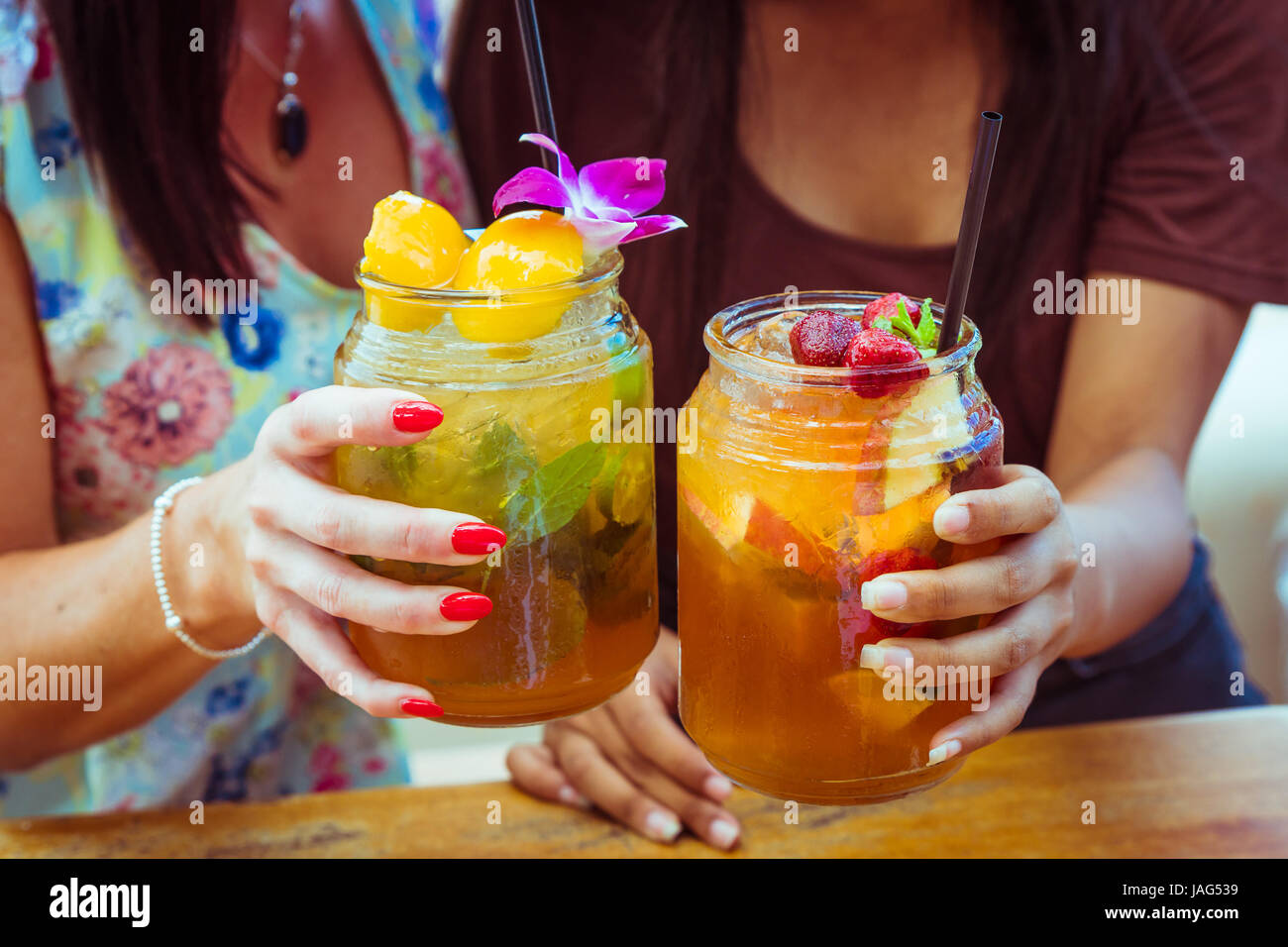 Portrait de deux femmes en robes colorées clink lunettes avec fraise rafraîchissant cocktail apple avec de la chaux et de pêche menthe cocktail froid Banque D'Images