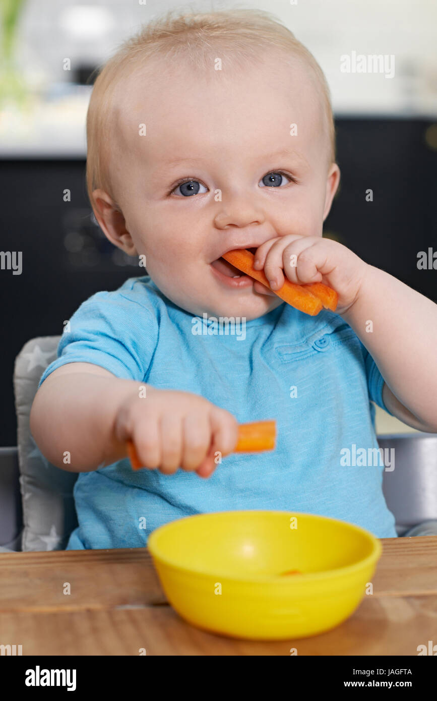 Heureux enfant assis à table en train de manger les carottes fraîches Banque D'Images