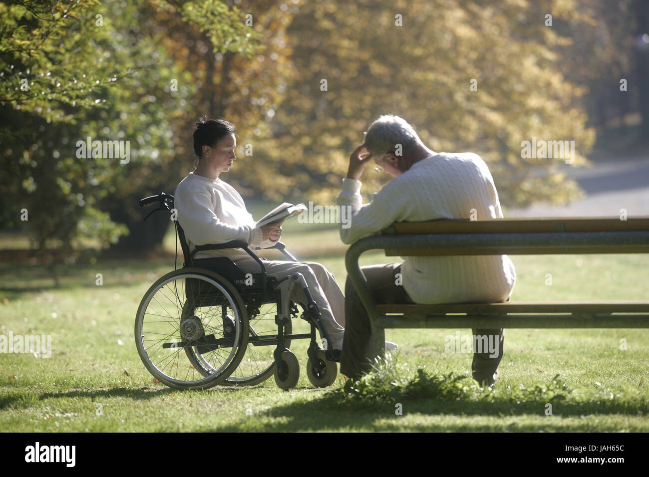 Femme de l'invalide en fauteuil lit,livre,homme sur banc de parc, Banque D'Images