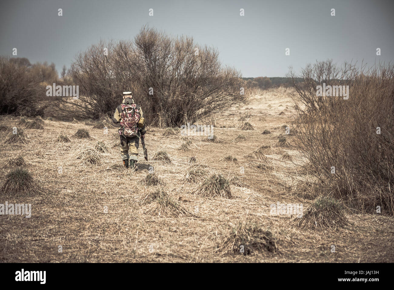 L'homme chasseur de camouflage avec fusil en zone rurale avec de l'herbe sèche et arbustes durant la chasse Banque D'Images