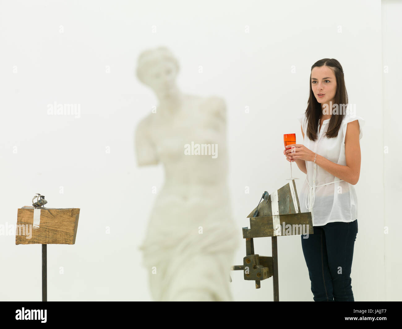 Young caucasian woman standing en face d'une œuvre d'art, tenant un verre de vin dans sa main, parlant, dans un musée d'art Banque D'Images