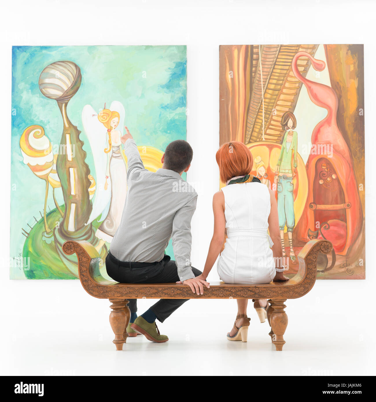 Young caucasian couple assis sur un banc en bois dans une galerie d'art en montrant de la peinture Banque D'Images