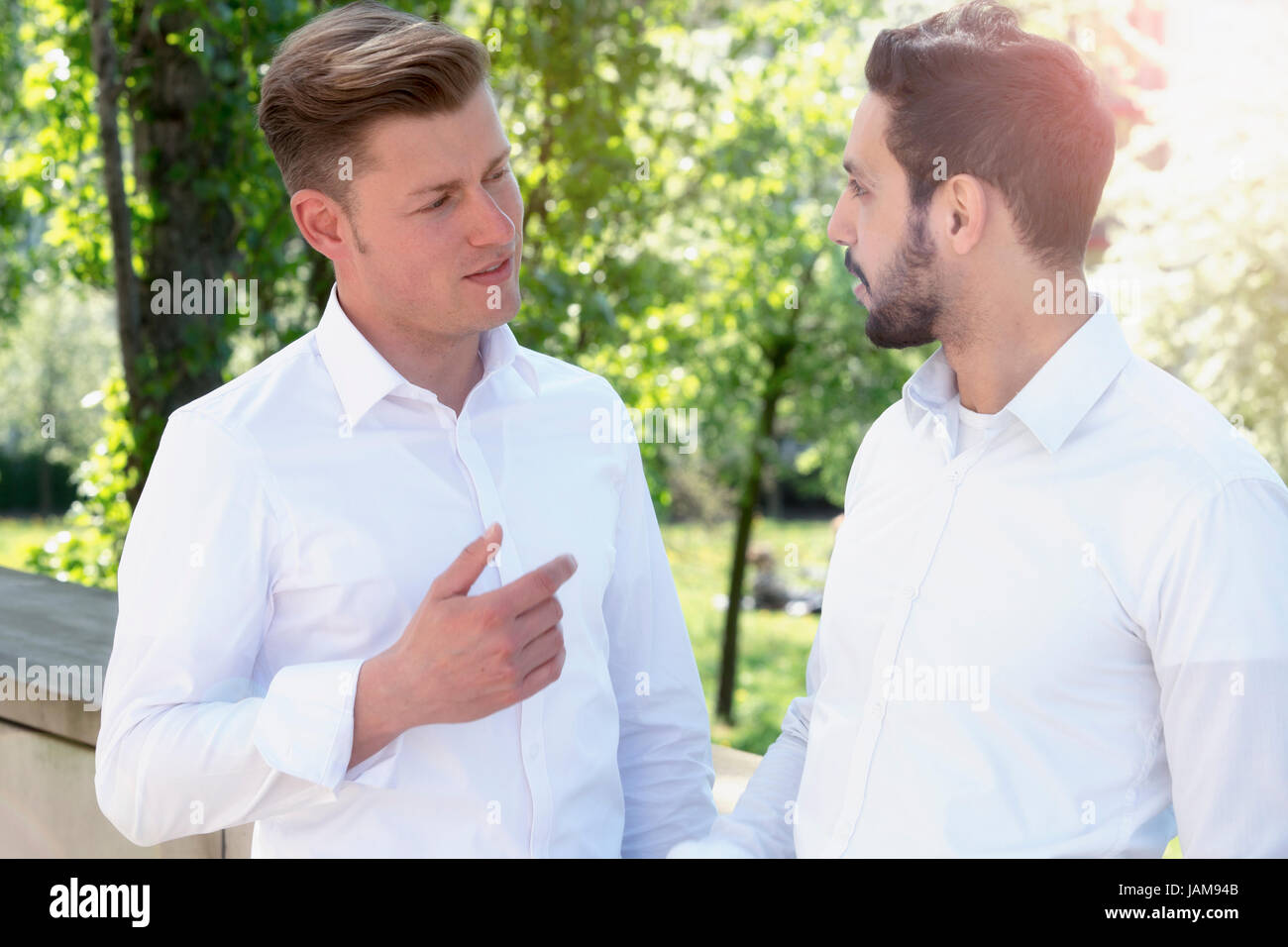 Deux jeunes hommes en chemise blanche d'avoir une conversation à l'extérieur dans le parc Banque D'Images
