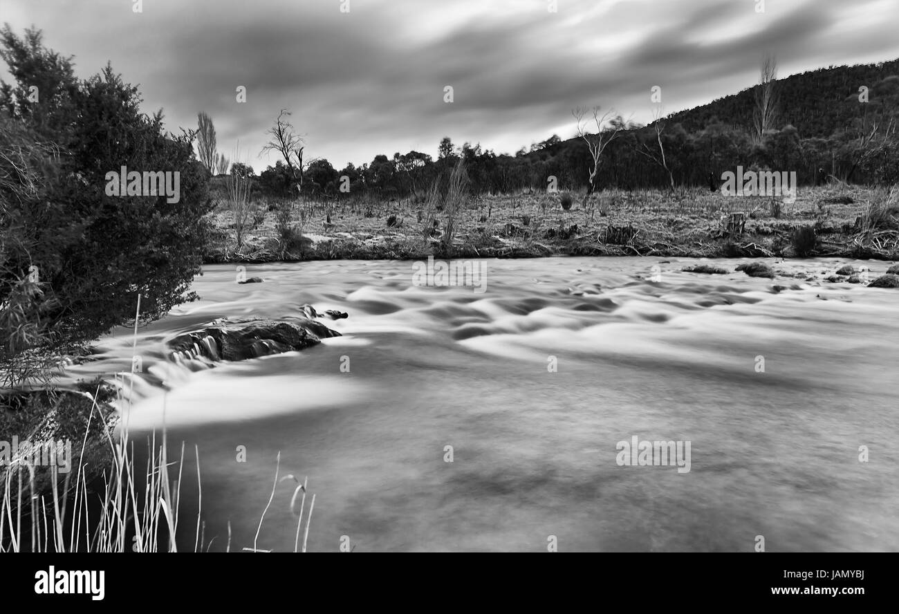 Noir blanc de Thredbo floue des radiers sur la rivière au coucher du soleil entre collines et montagnes dans le parc national de Kosciuszko. Banque D'Images