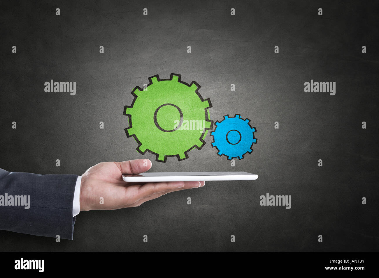 Businessman hand holding digital tablet avec engrenages concept sur tableau noir Banque D'Images