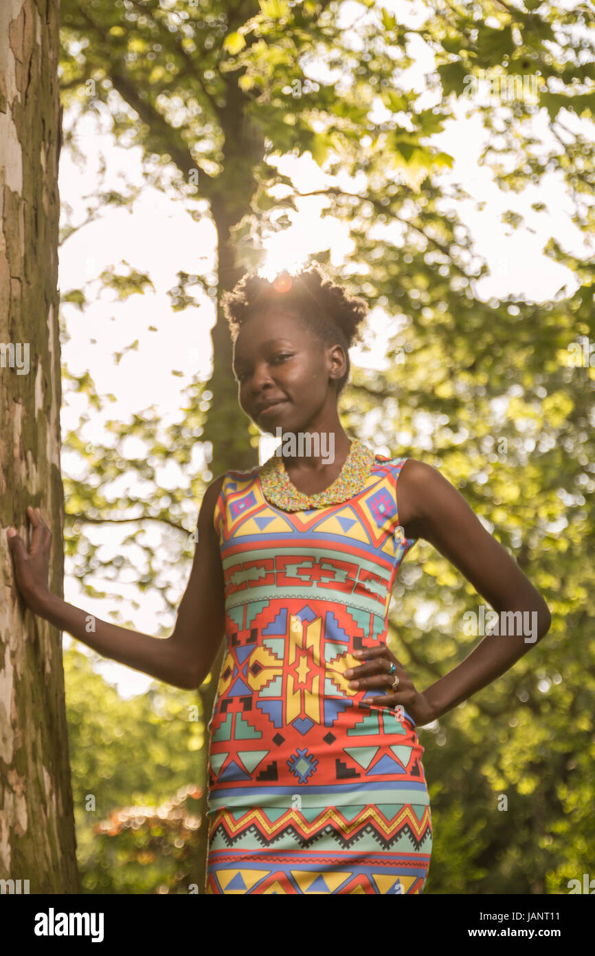 L'un, jeune adulte, black african american woman à 29 ans, l'article portrait enjoué, s'appuyant sur arbre, journée ensoleillée à l'extérieur, derrière la cime, low angle Banque D'Images
