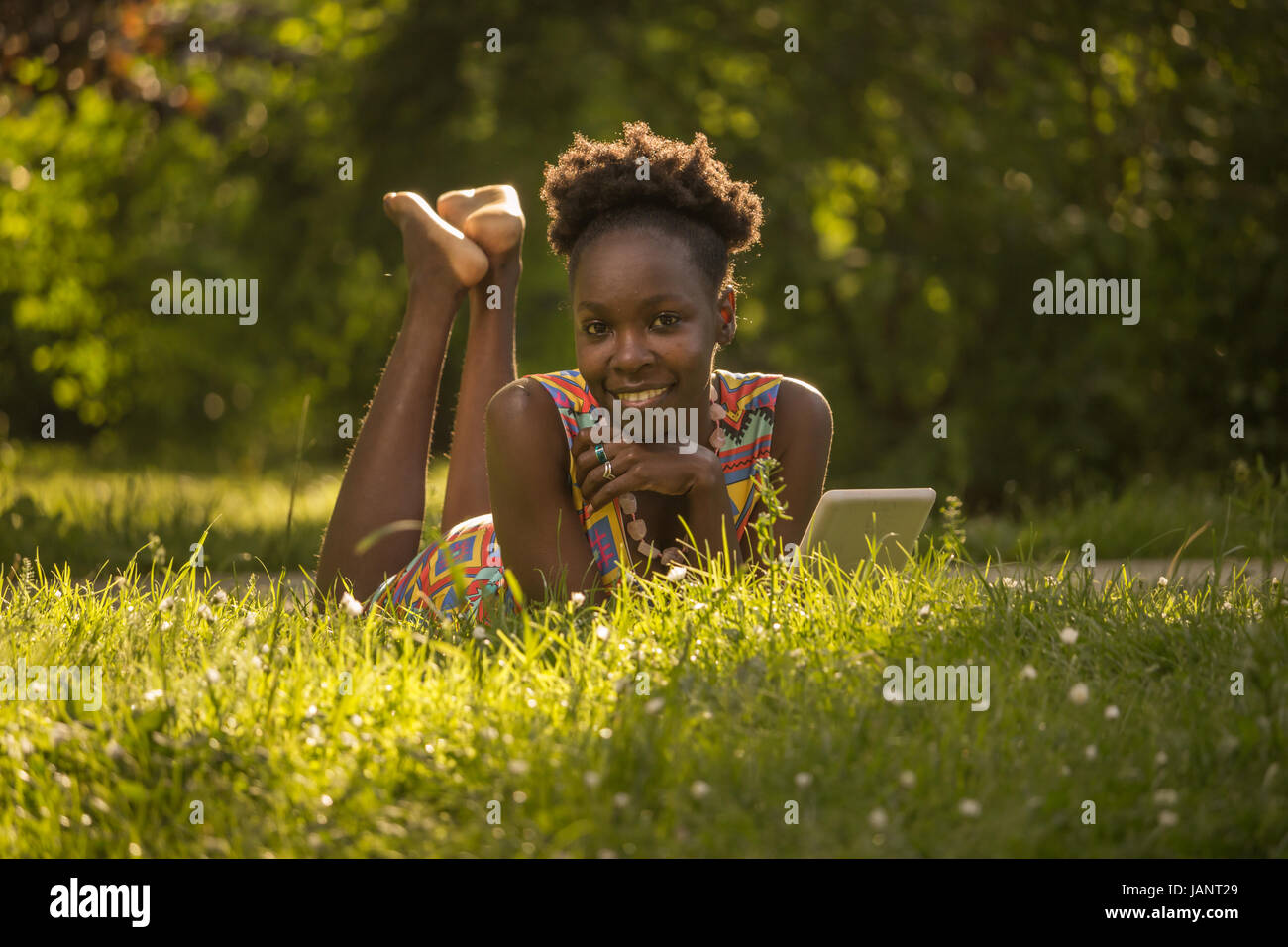 L'un, jeune adulte, black african american woman happy smiling bénéficiant à 29 ans, fixant lying on grass, Tablette de lecture à la recherche d'appareil photo, à l'extérieur p Banque D'Images