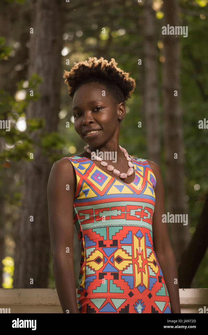 L'un, jeune adulte, black african american happy smiling woman 29 ans, debout, à la recherche d'appareil photo, dehors parc nature, journée ensoleillée, low angle view Banque D'Images