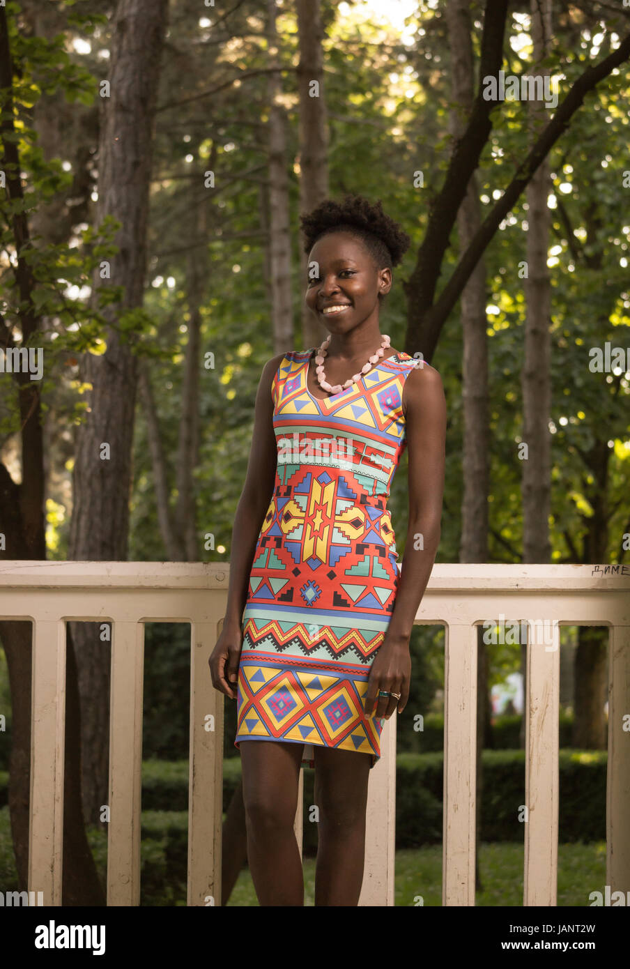 L'un, jeune adulte, black african american happy smiling woman 29 ans, debout, à la recherche d'appareil photo, dehors parc nature de clôture, journée ensoleillée, le port Banque D'Images
