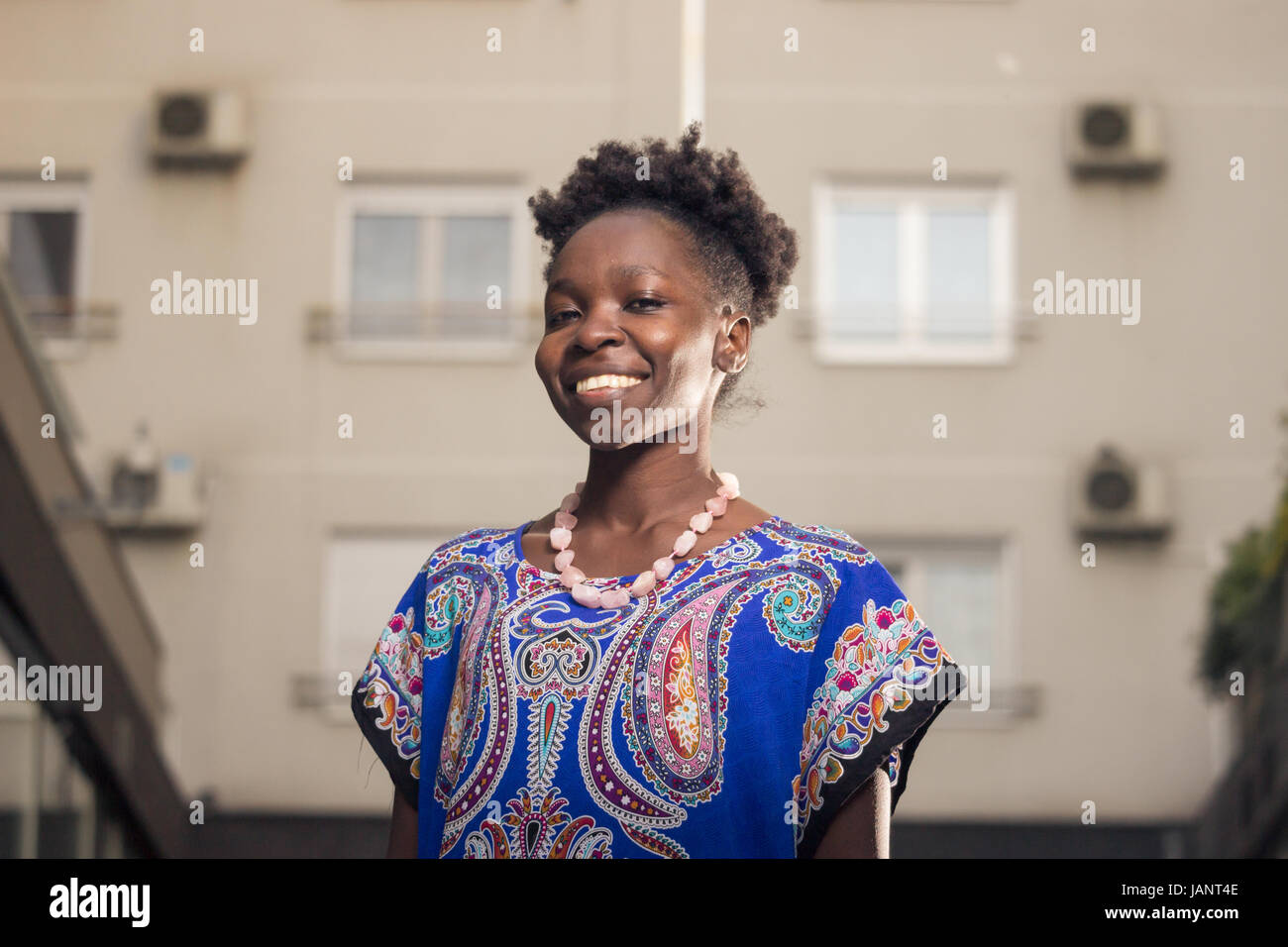 L'un, jeune adulte, black african american woman, 29 ans, happy smiling, tête et épaules, derrière les bâtiments, à la recherche d'appareil photo, low angle vi Banque D'Images