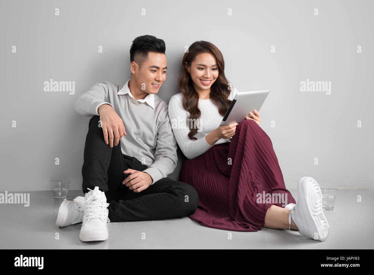 Pretty smiling asian couple dans l'amour ensemble assis sur le plancher bénéficiant using digital tablet Banque D'Images