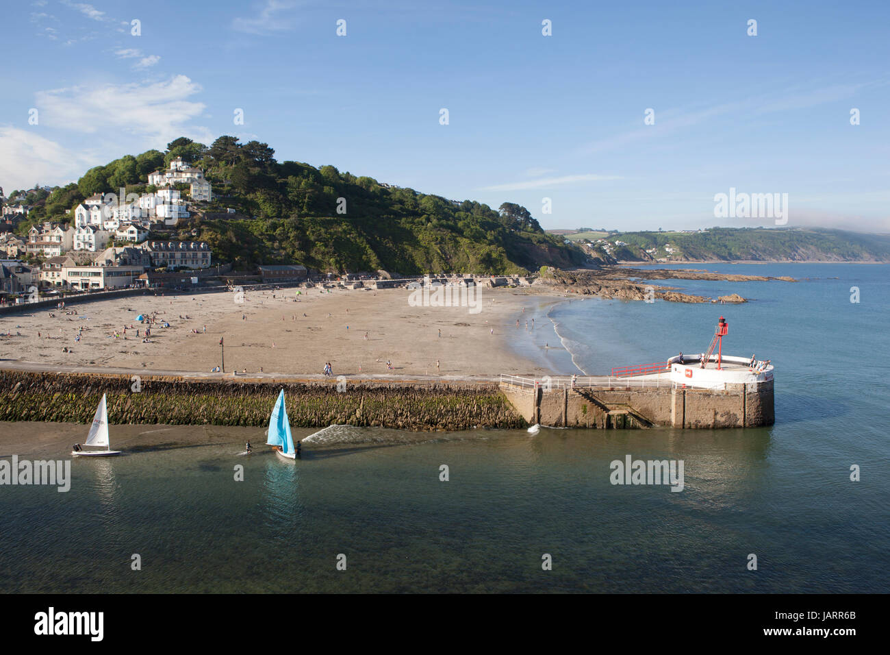 Petits dériveurs avec voiles multicolores partir en mer à Looe, Cornwall. Le banjo pier et plage sont au premier plan et la ville est vue sur la colline. Banque D'Images