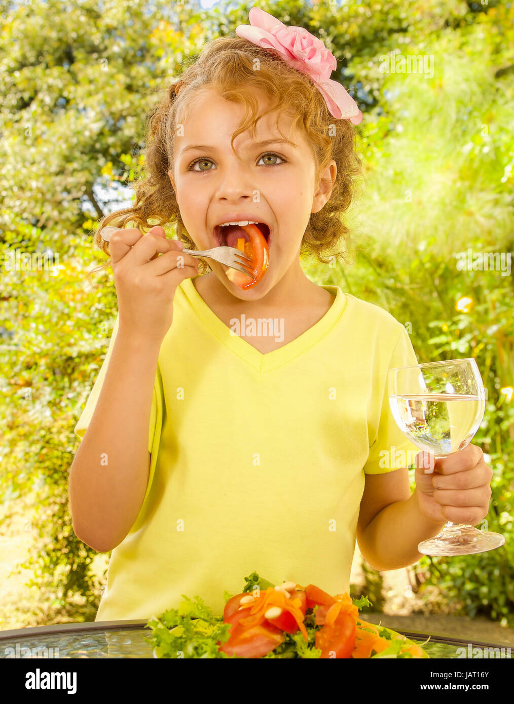 Belle jeune fille, portant un t-shirt jaune de manger une salade de tomates et de sa holding glass of water, dans un jardin historique. Banque D'Images