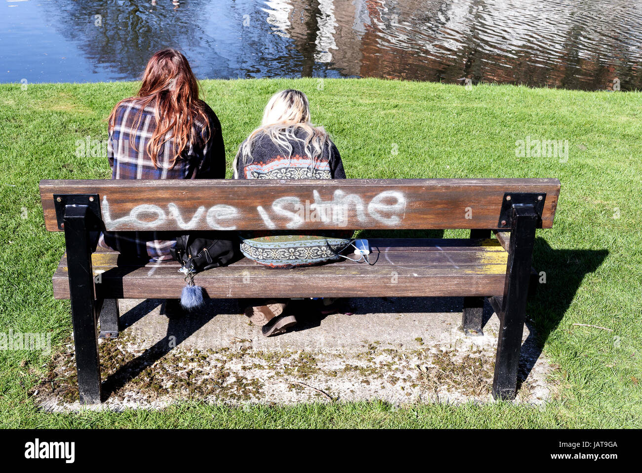 Deux jeunes femme assise à un banc d'amour est l'étiquette sur l'arrière de l'assise en bois Banque D'Images