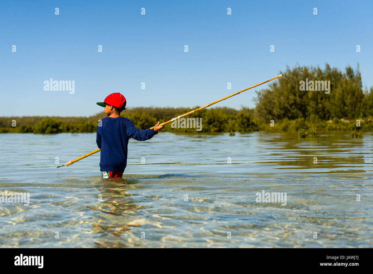 Un garçon autochtone utilise une longue lance barbelée de chasser pour des raies dans les eaux peu profondes du lagon. Banque D'Images