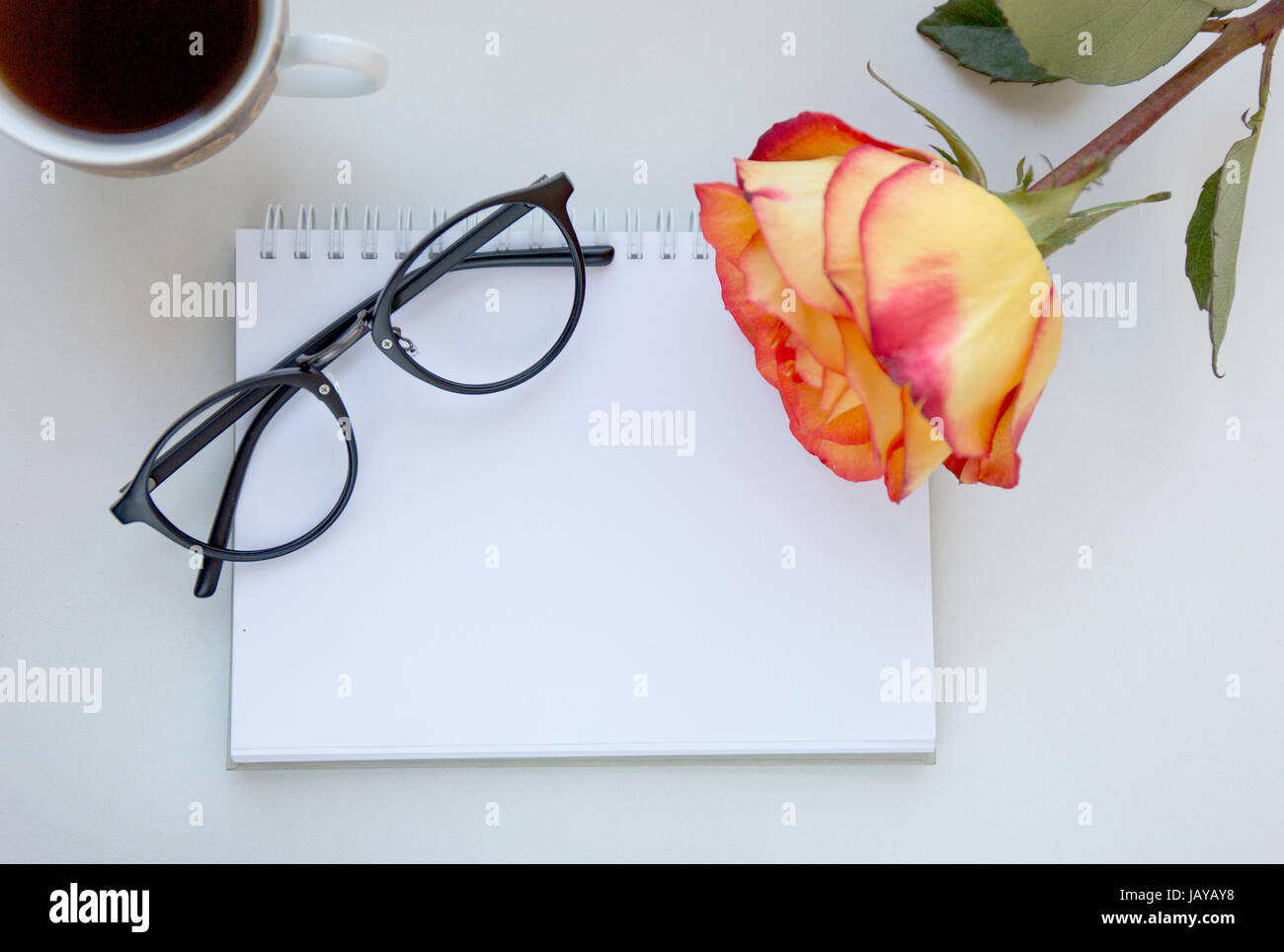La maquette de l'ordinateur portable de l'art en rouge et jaune rose, verres et tasse de café noir. Vue d'en haut. Place pour le texte. Des fleurs Banque D'Images