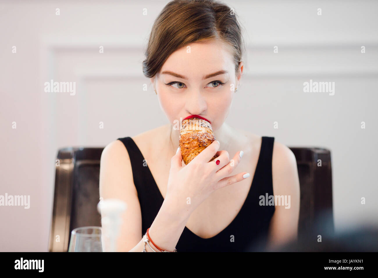 Woman biting dans un croissant dans un café intérieur Banque D'Images