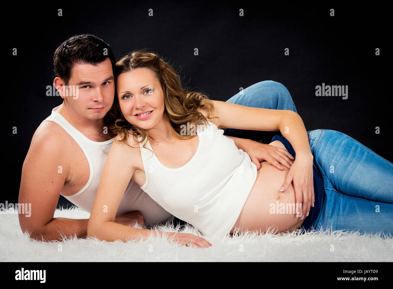 La grossesse couple lying hugging sur fond noir Banque D'Images