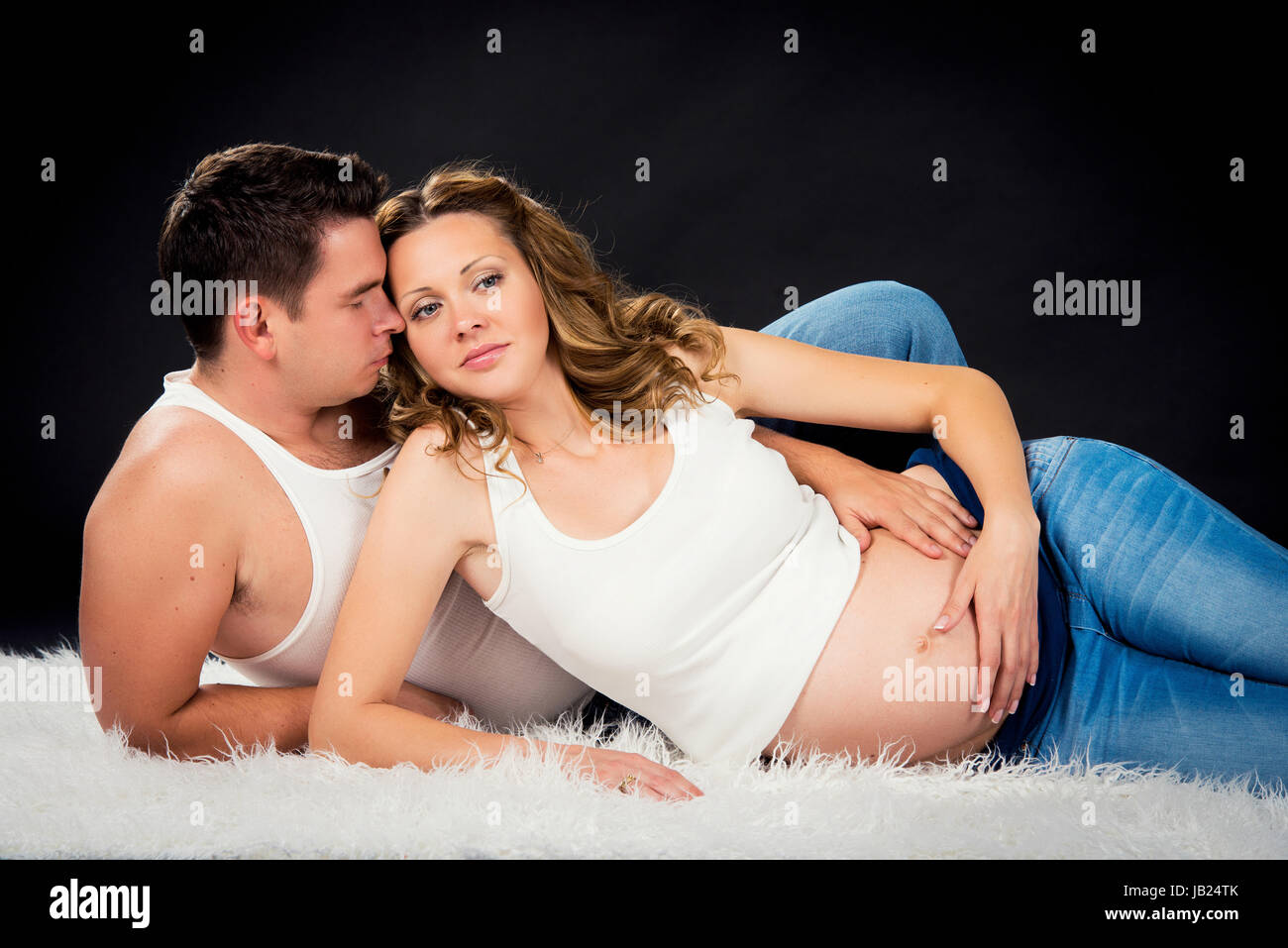 La grossesse couple lying hugging sur fond noir Banque D'Images