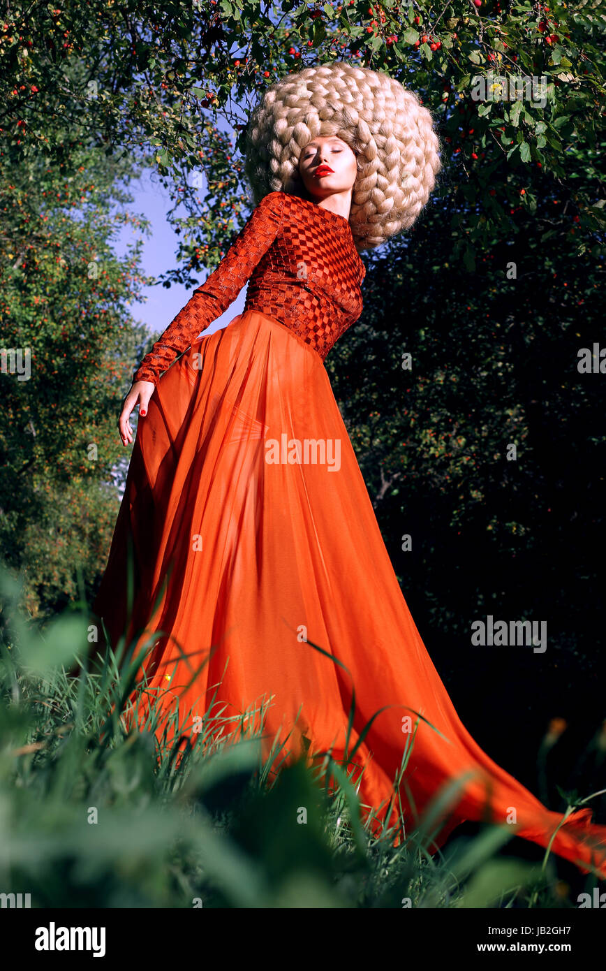 La fantaisie. Femme stylisée artistique dans le quartier branché de robe rouge et grosse perruque frisée Banque D'Images