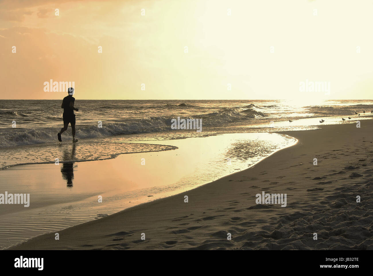 Homme qui court à travers les vagues vers le soleil aveuglant Banque D'Images