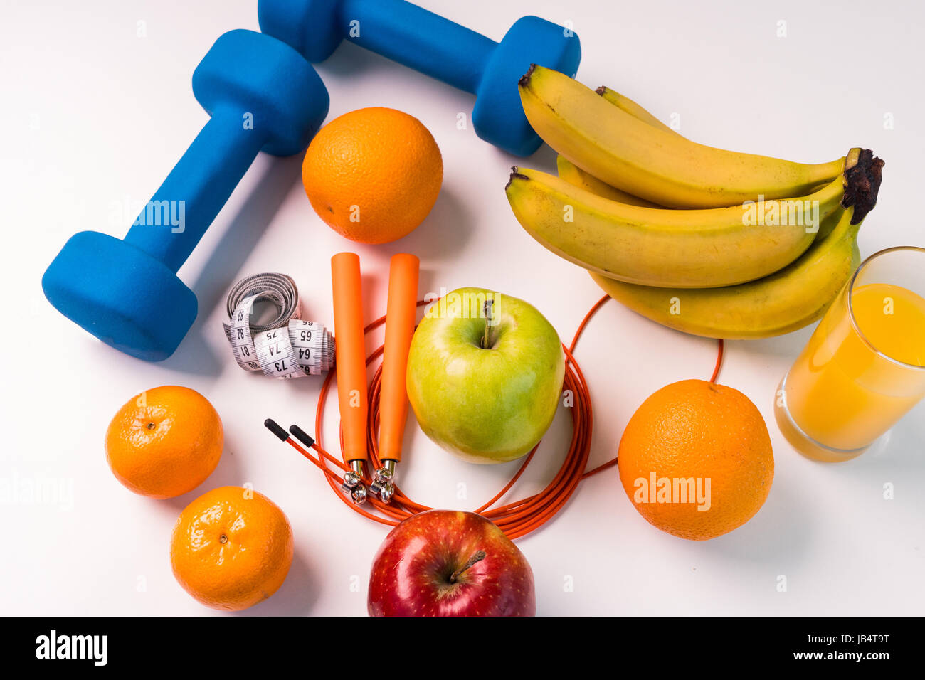 Concept de saine alimentation. Corde à sauter, haltères, bananes, oranges, ruban à mesurer la taille, des oranges, pomme rouge, pomme verte, jus d'orange sur un onglet blanc Banque D'Images