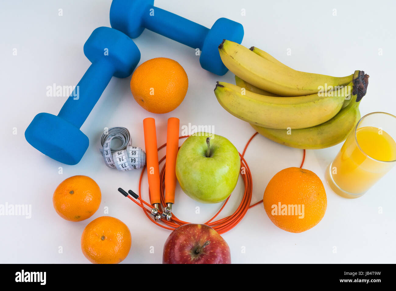 Concept de saine alimentation. Corde à sauter, haltères, bananes, oranges, ruban à mesurer la taille, des oranges, pomme rouge, pomme verte, jus d'orange sur un onglet blanc Banque D'Images