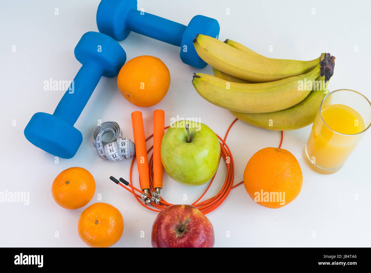 Concept de saine alimentation. Corde à sauter, haltères, bananes, oranges, ruban à mesurer la taille, des oranges, pomme rouge, pomme verte, jus d'orange sur un onglet blanc Banque D'Images