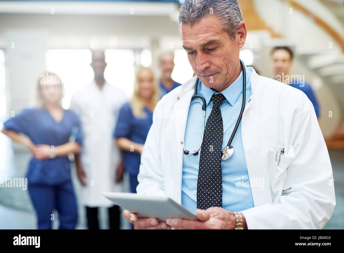 Médecin à l'hôpital à la recherche à tablette. Comité permanent de l'équipe médicale en arrière-plan. Banque D'Images