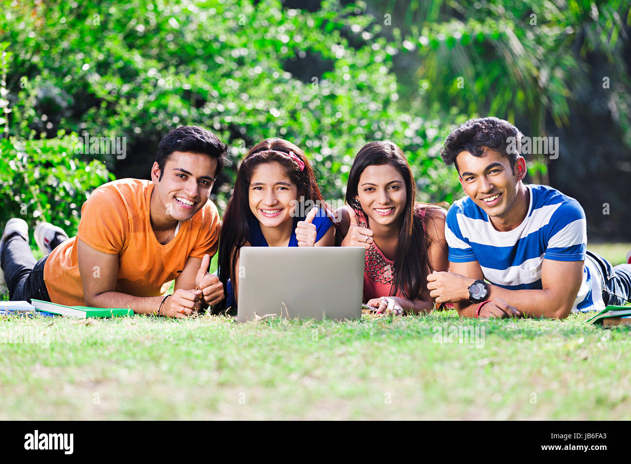 4 Indian college filles et garçons à l'aide d'amis et d'ordinateur portable showing Thumbs up étudier au park Banque D'Images