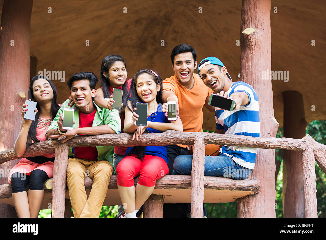 Groupe indien adolescents filles et garçons assis et banc en bois montrant téléphone mobile en park Banque D'Images