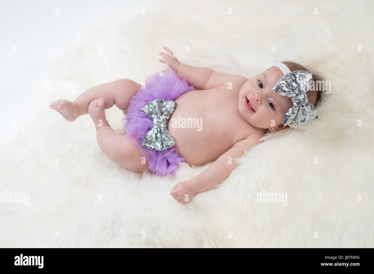 Portrait d'un bébé de quatre mois girl wearing frilly, violet et argent, un sequin, bow serre-tête. Tourné en studio sur un tapis en peau de mouton. Banque D'Images