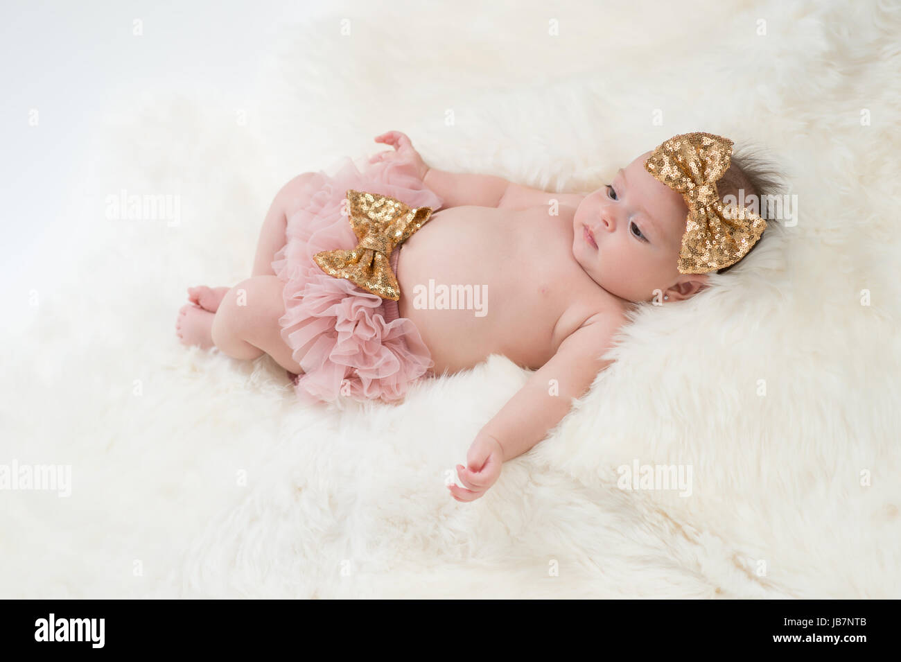Portrait d'un bébé de quatre mois girl wearing frilly, rose et or, un sequin, bow serre-tête. Tourné en studio sur un tapis en peau de mouton. Banque D'Images