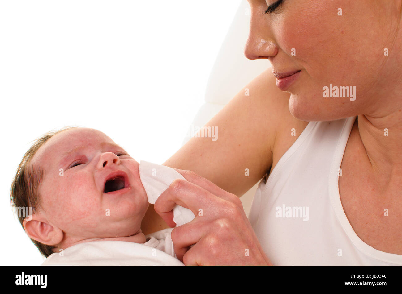 Erwachsene Eine Frau mit weißem Shirt hält einen gekleideten Säugling les weiß auf und zärtlich bras tupft ihm mit einem Tuch den Mund sauber, freigestellt Hintergrund weißem vor. Banque D'Images