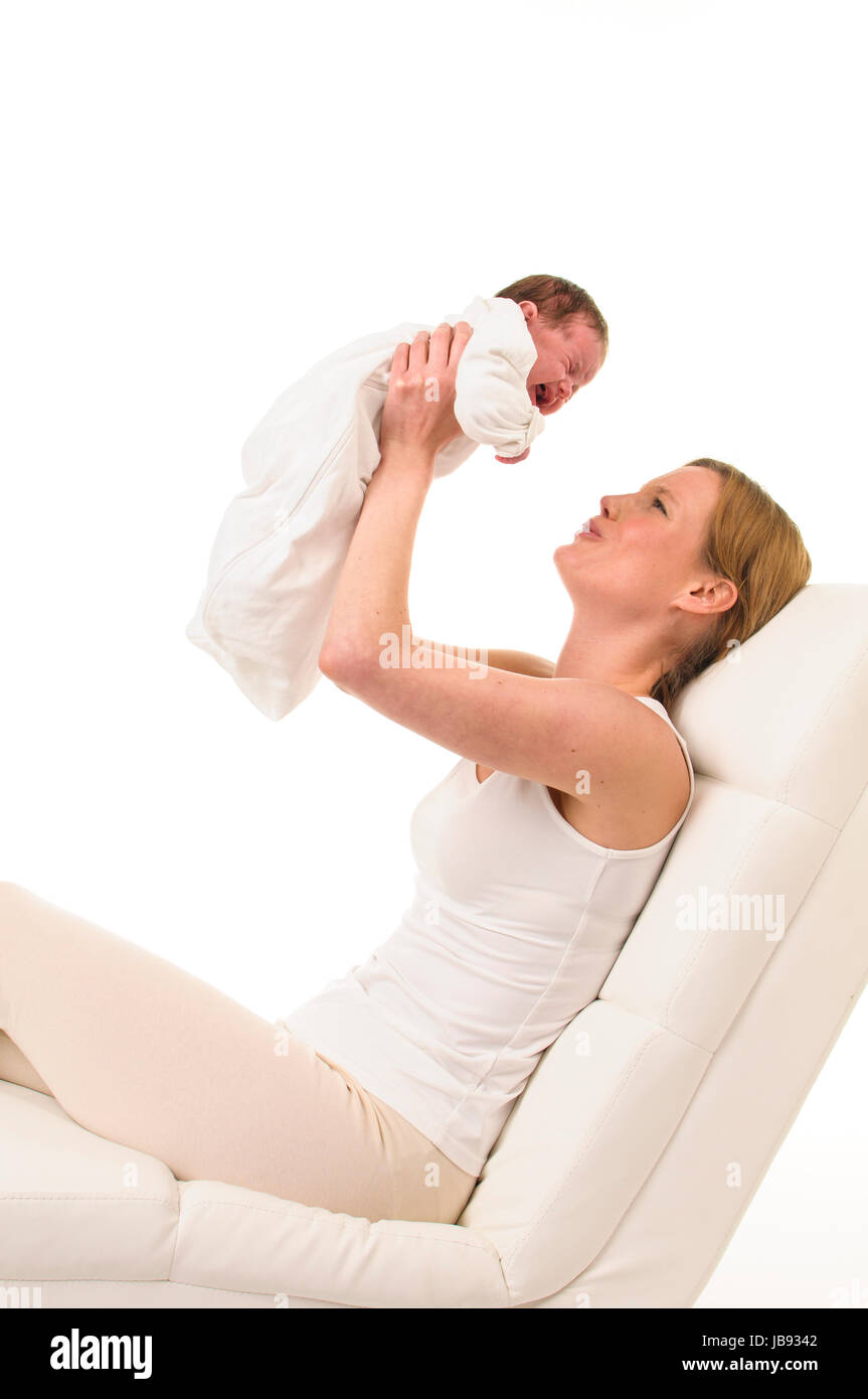 Erwachsene Eine Frau mit weißem Shirt liegt auf einer hält einen Liège weißer bär und weiß les gekleideten Säugling vor sich in die Luft, freigestellt Hintergrund weißem vor. Banque D'Images