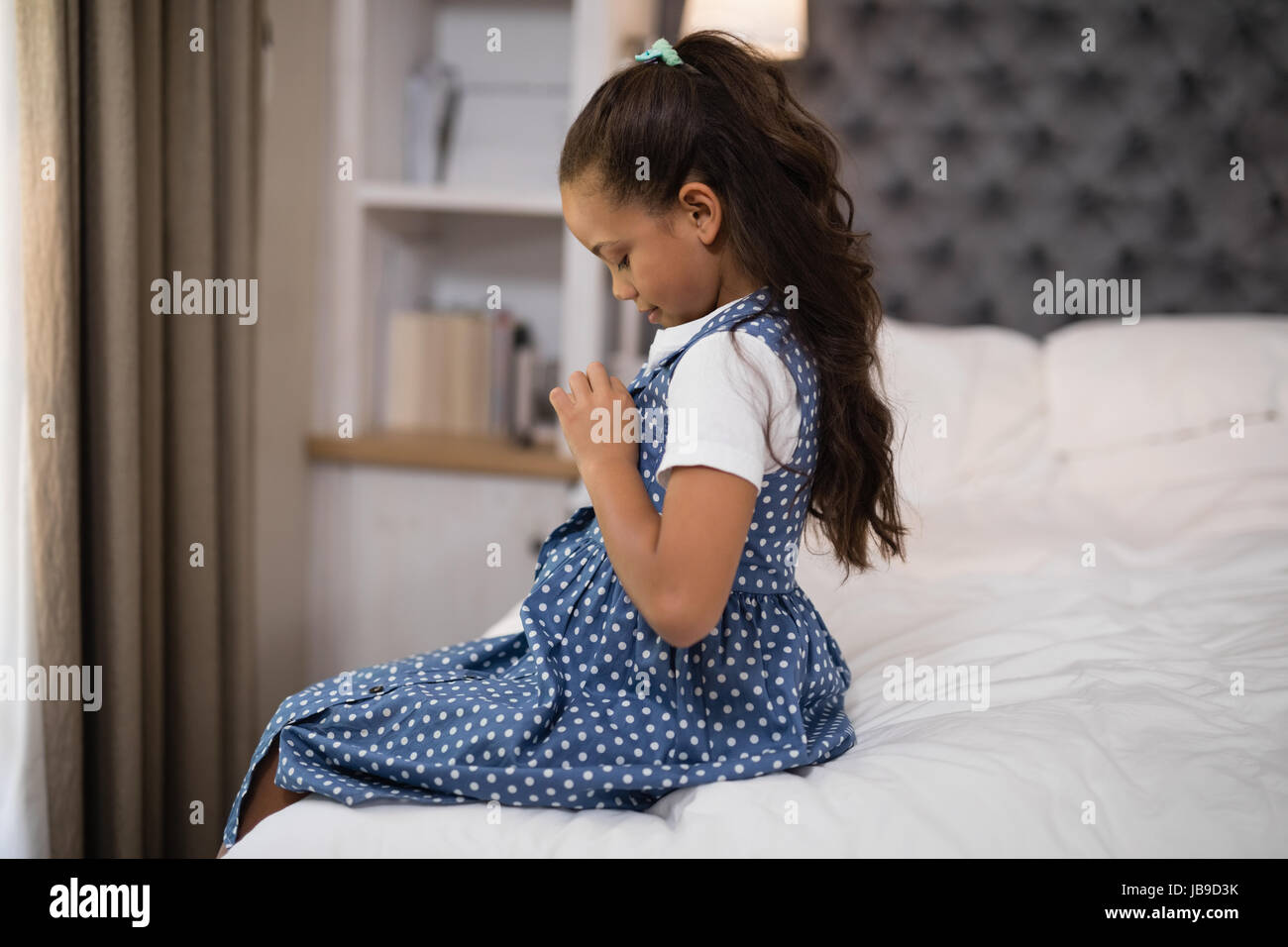 Vue latérale du girl dressing up while sitting on bed at home Banque D'Images