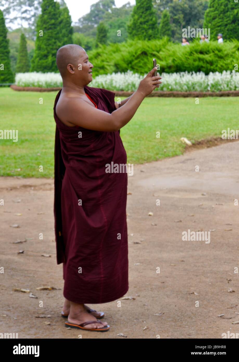 Un moine bouddhiste en robes marron signifie prendre une avec son téléphone portable selfies dans un parc du Myanmar Banque D'Images