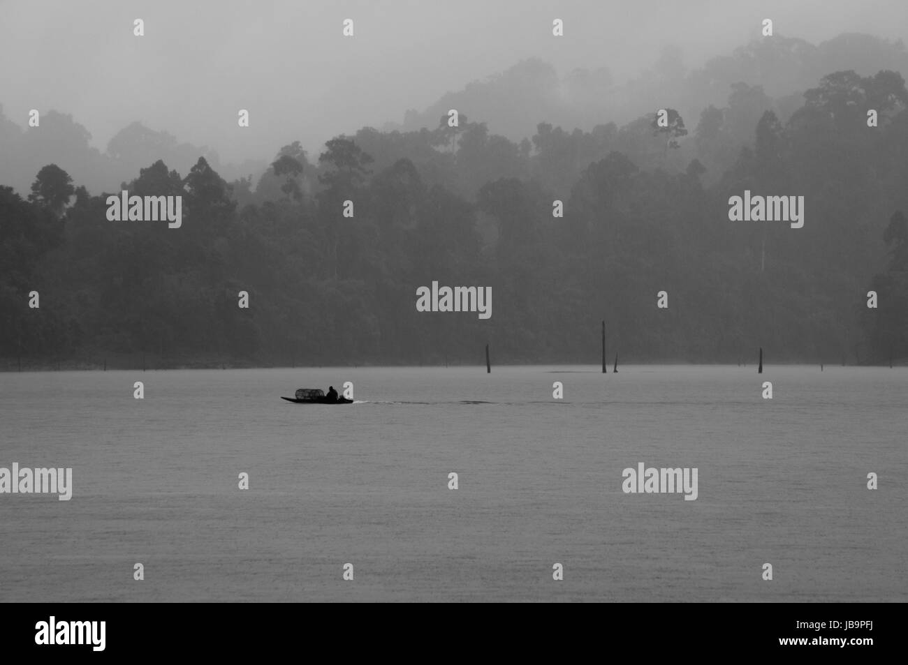 Un petit bateau naviguant sur le lac Cheow Lan dans une pluie tropicale (noir et blanc) Banque D'Images