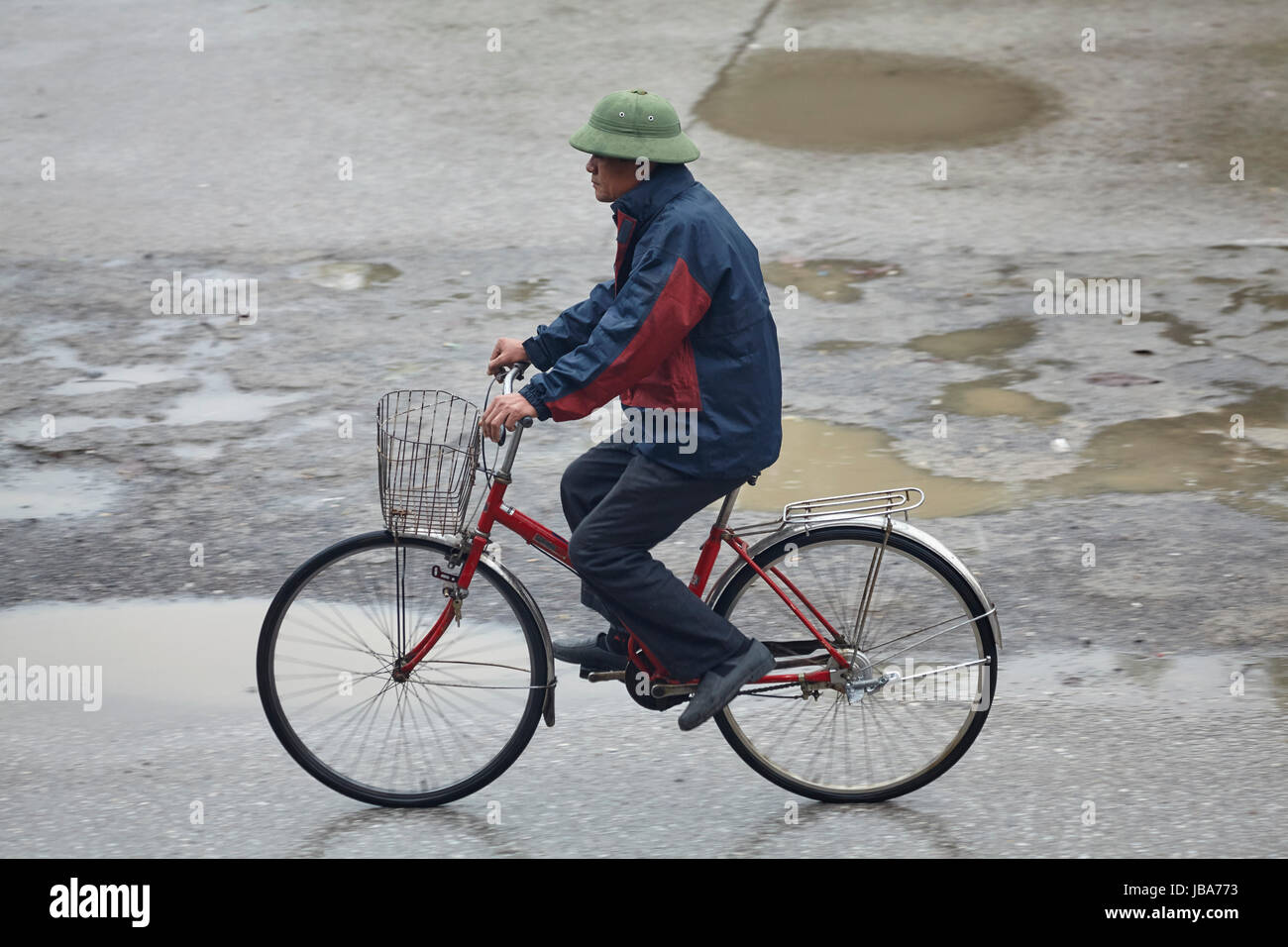 Vieil homme à vélo dans la pluie, Ninh Binh, Vietnam Banque D'Images