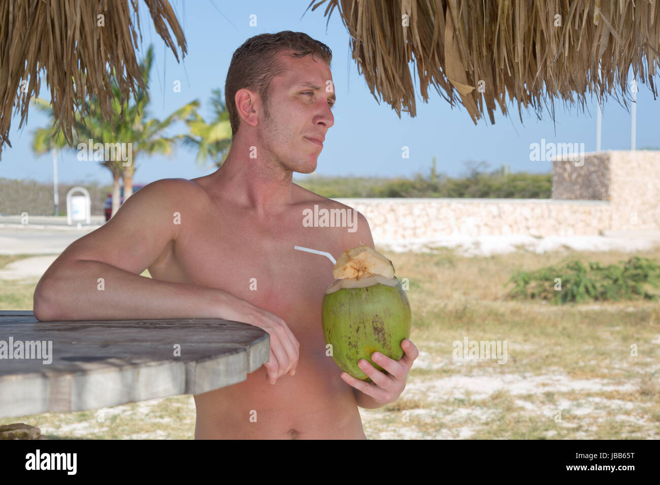 Junger Mann trinkt im Urlaub am Strand aus einer Kokosnuss Banque D'Images