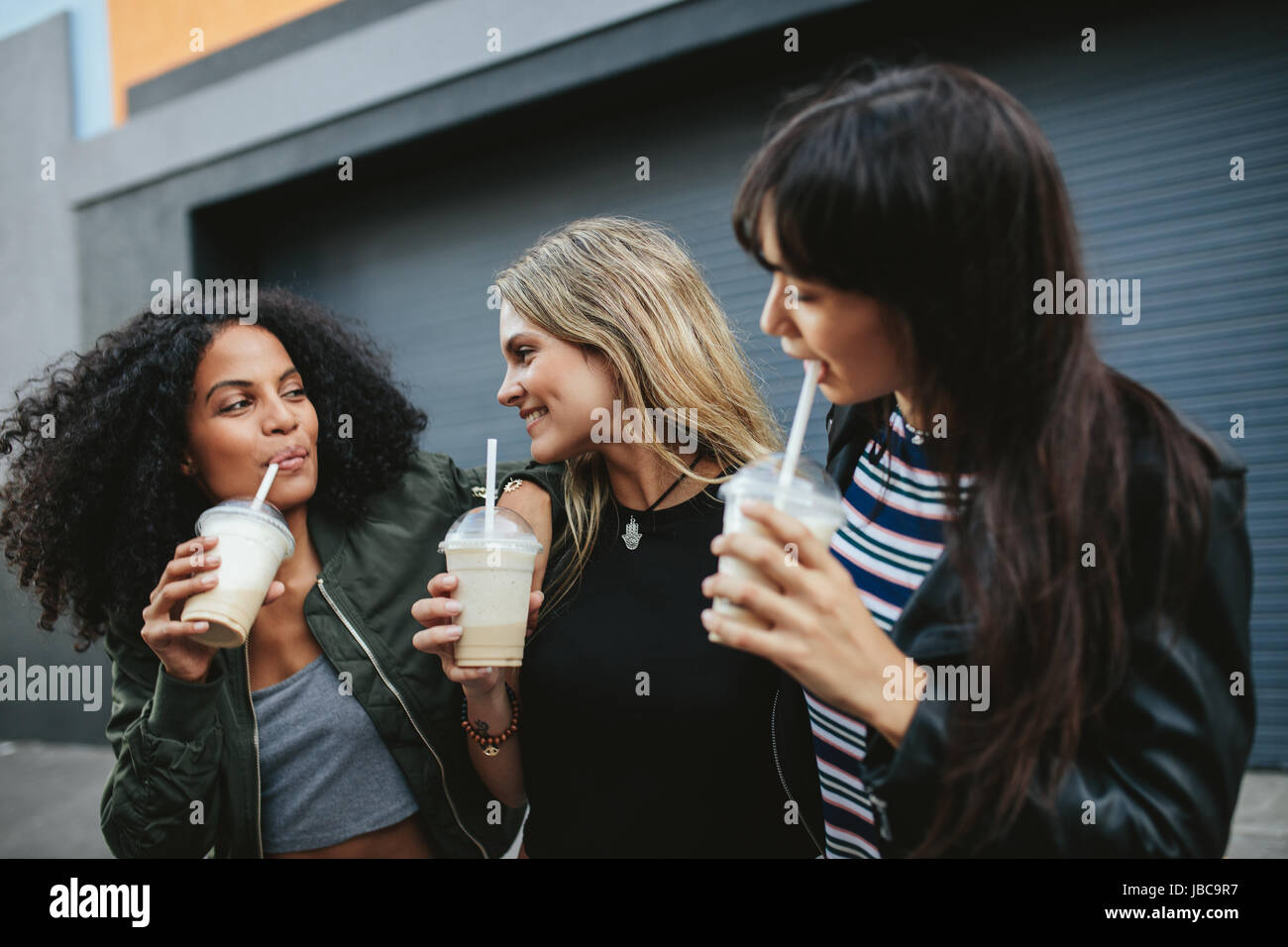 Tourné de trois jeunes femmes de boire du café de glace sur la rue de la ville. Groupe diversifié d'amies ayant café glace à l'extérieur. Banque D'Images