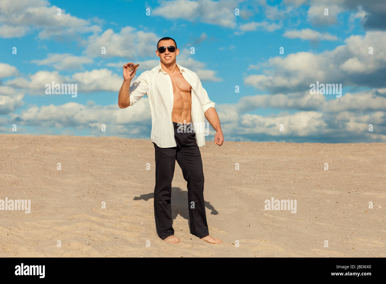 L'homme avec un cigare dans la main est pieds nus sur le sable dans le désert. Il portait une chemise blanche et un pantalon. Banque D'Images