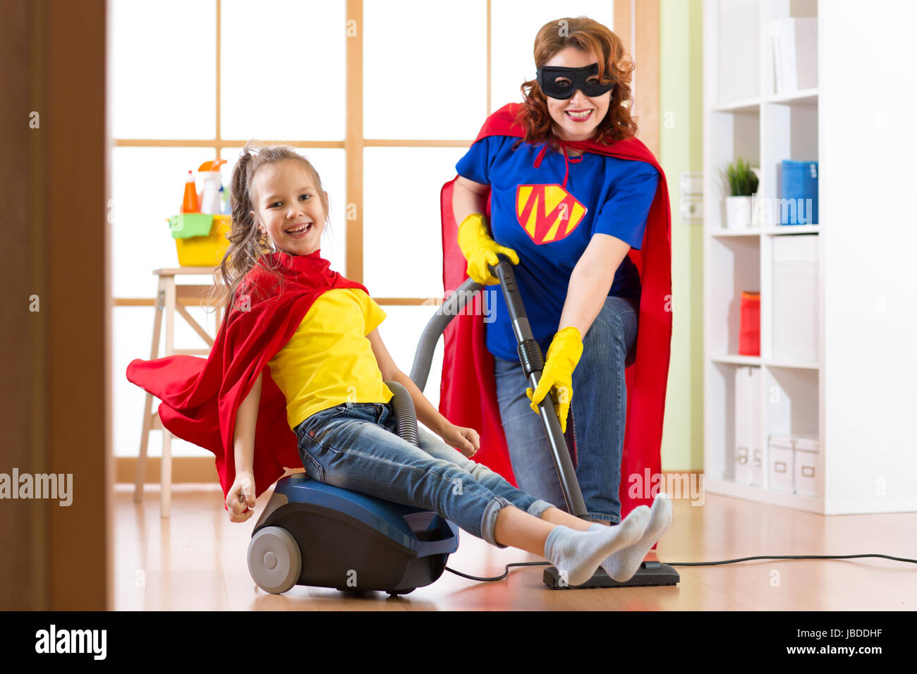 Jeune fille et sa mère Superhero costumes portés par... Enfant mignon et femme font l'assistant de nettoyage prix et avoir un plaisir. Banque D'Images
